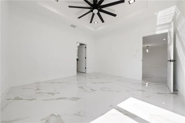 Unfurnished room with visible vents, baseboards, a raised ceiling, a ceiling fan, and marble finish floor