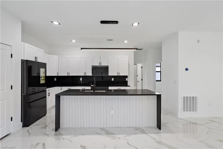 Kitchen with tasteful backsplash, visible vents, freestanding refrigerator, dark countertops, and marble finish floor