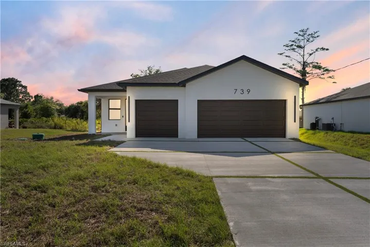 View of front of house featuring an attached garage, a front lawn, driveway, and stucco siding