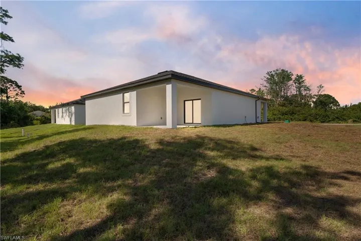 Back of property at dusk with an outbuilding, stucco siding, a pole building, and a lawn