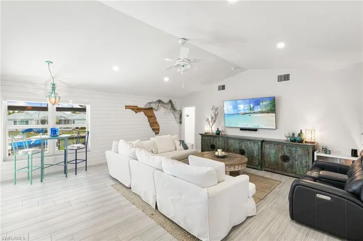 Living room with light wood-type flooring, ceiling fan, a chandelier, and wood walls