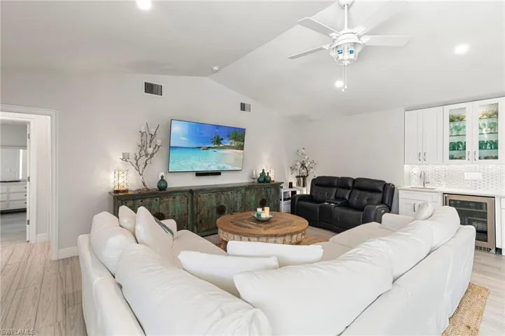 Living room featuring wine cooler, ceiling fan, light wood-type flooring, and bar area