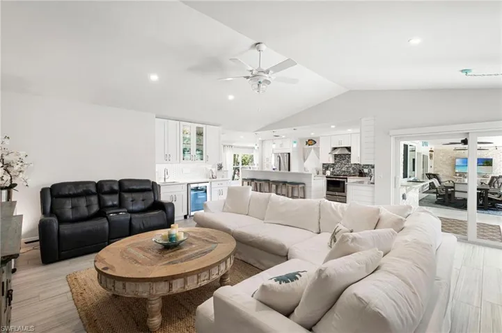 Living room featuring ceiling fan, light wood-style flooring, beverage cooler, vaulted ceiling, and bar