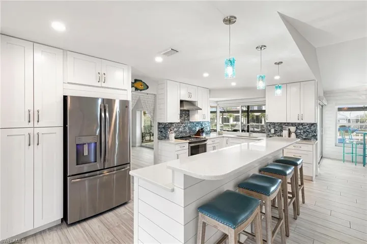 Kitchen with stainless steel appliances, white cabinetry, hanging light fixtures, a kitchen breakfast bar, and light stone counters