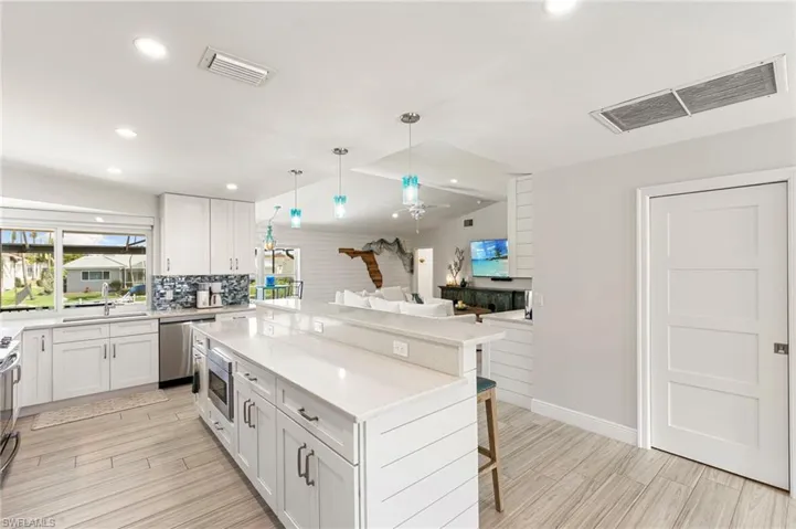 Kitchen featuring a kitchen breakfast bar, white cabinetry, a kitchen island, wood tiled floors, and light stone countertops