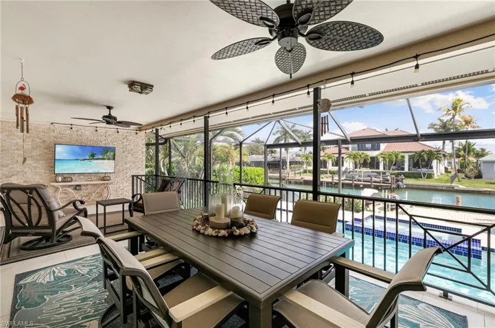 View of patio featuring ceiling fan, a sunroom, a water view, outdoor dining area, and an outdoor pool