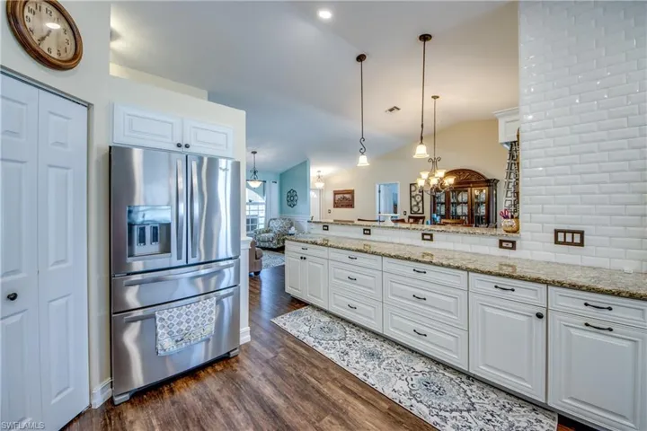 Kitchen featuring stainless steel fridge with ice dispenser, dark wood-type flooring, white cabinets, decorative light fixtures, and vaulted ceiling