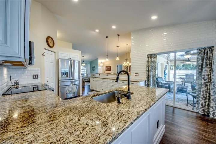 Kitchen featuring dark hardwood / wood-style flooring, backsplash, stainless steel refrigerator with ice dispenser, pendant lighting, and sink