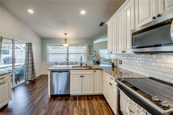Kitchen with appliances with stainless steel finishes, dark hardwood / wood-style floors, kitchen peninsula, backsplash, and sink