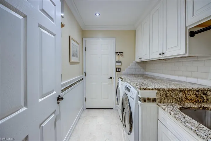 Laundry area with crown molding, washing machine and dryer, light tile flooring, and cabinets