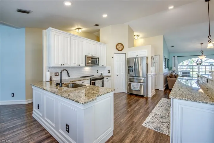 Kitchen featuring dark hardwood / wood-style floors, tasteful backsplash, hanging light fixtures, sink, and appliances with stainless steel finishes