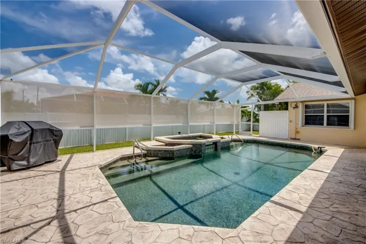 View of pool with a patio area, area for grilling, glass enclosure, and an in ground hot tub