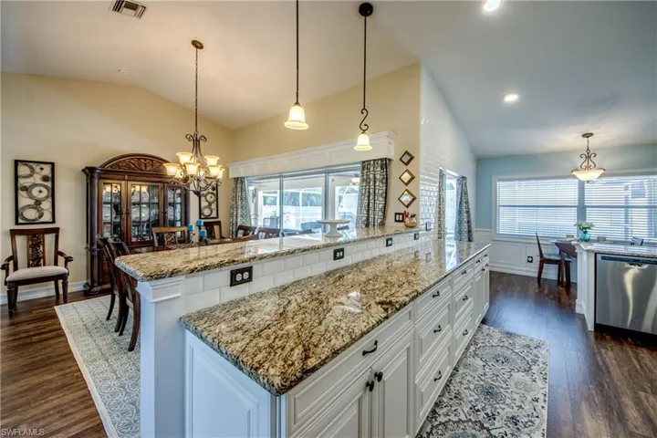 Kitchen with light stone countertops, stainless steel dishwasher, white cabinets, dark hardwood / wood-style floors, and decorative light fixtures