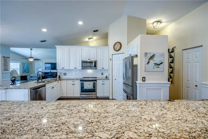 Kitchen with white cabinets, kitchen peninsula, backsplash, ceiling fan, and appliances with stainless steel finishes