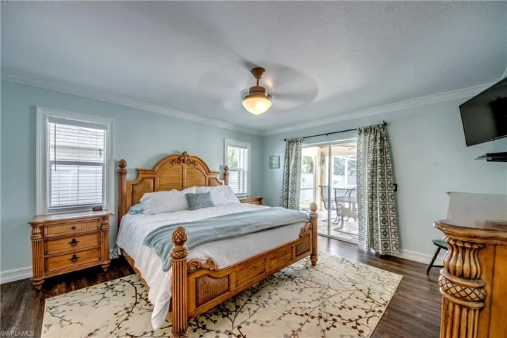 Bedroom featuring dark wood-type flooring, ornamental molding, ceiling fan, and access to exterior