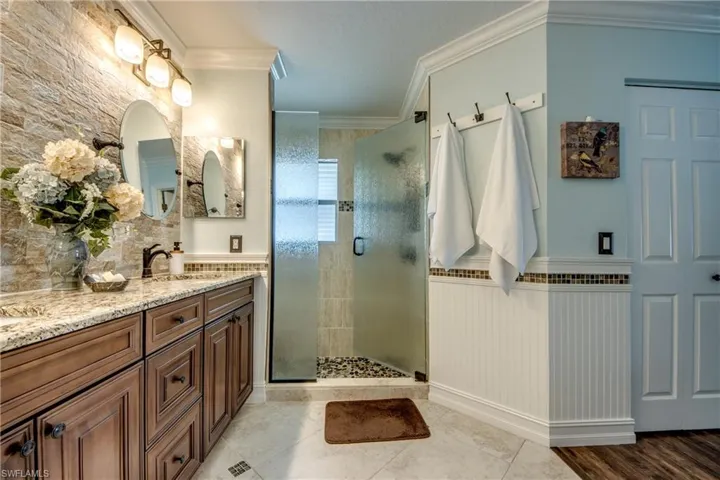 Bathroom with crown molding, a shower with door, tile flooring, and double vanity