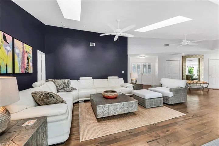 Living room featuring a ceiling fan, a skylight, lofted ceiling, and hardwood / wood-style flooring