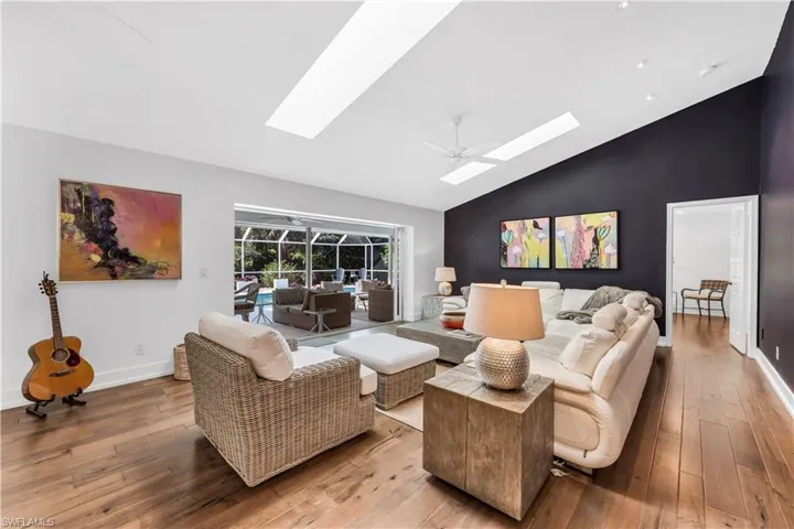 Living area with wood-type flooring, a ceiling fan, a sunroom, vaulted ceiling, and a skylight