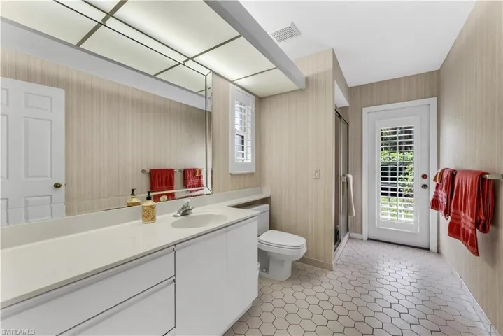 Bathroom featuring plenty of natural light, vanity, a shower stall, and wallpapered walls. Exits to pool area.