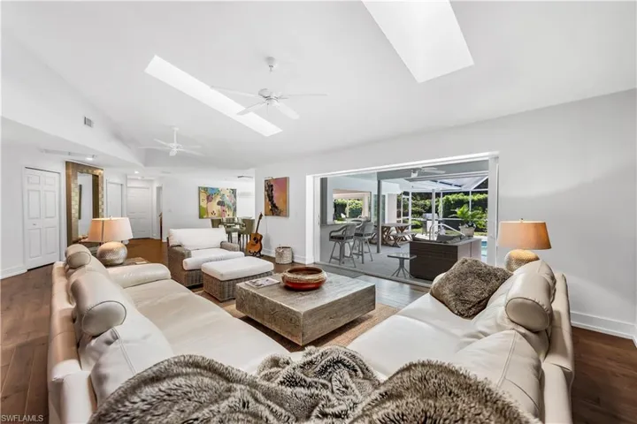 Great room featuring a ceiling fan, hardwood / wood-style flooring, a skylight, a sunroom, and lofted ceiling