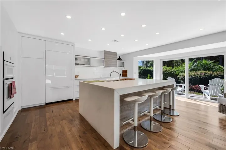 Kitchen featuring modern cabinets, a kitchen breakfast bar, light stone counters, dark wood-type flooring, and recessed lighting
