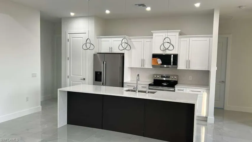 Kitchen with stainless steel appliances, light stone counters, white cabinetry, an island with sink, and recessed lighting