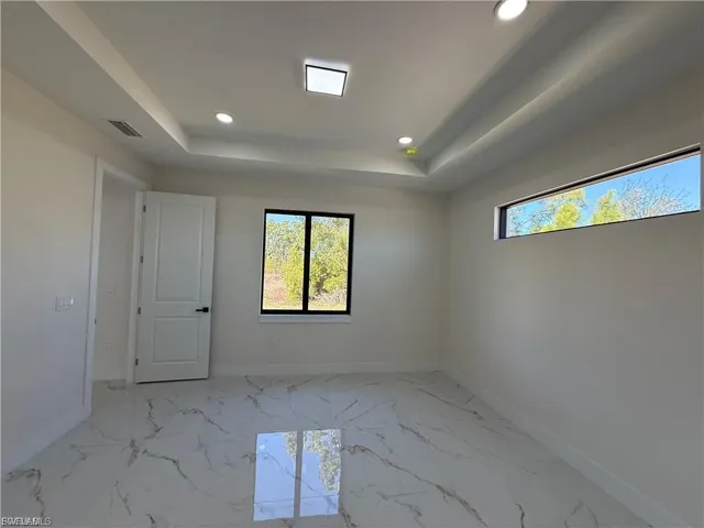 Empty room featuring light marble finish flooring, recessed lighting, and a raised ceiling