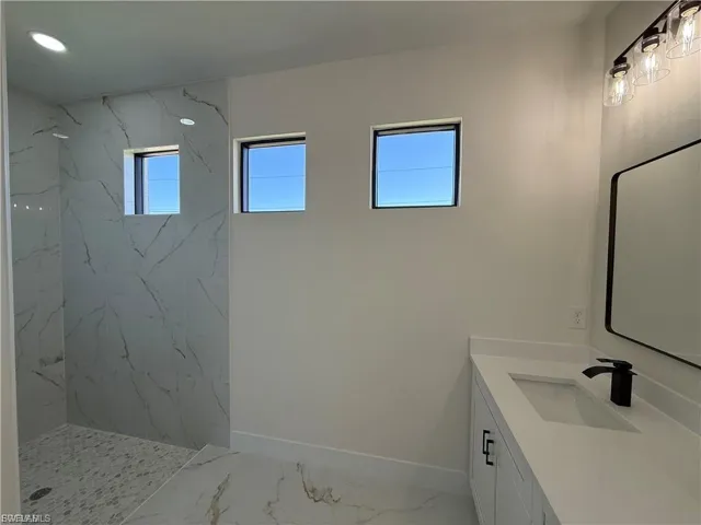 Bathroom with vanity, a marble finish shower, and light marble finish flooring