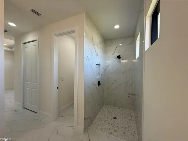 Bathroom featuring a marble finish shower, recessed lighting, light marble finish floors, and a closet