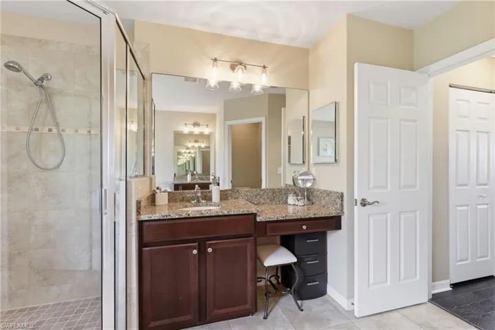 Bathroom featuring a glass-enclosed shower with tile surround, a vanity with a granite-style countertop, dark wood-finish cabinetry, and a full-width mirror