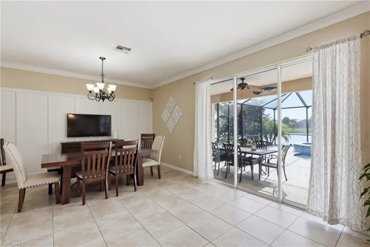 Spacious dining area featuring tile flooring, crown molding, a decorative chandelier, and a wall panel accent