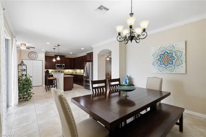 Open-concept space featuring a dining area with a chandelier, tile flooring, and a kitchen with dark wood-finish cabinetry, stainless steel appliances, and pendant lighting
