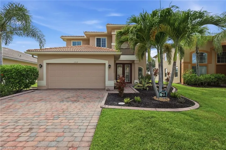 Stucco exterior with a tiled roof, paver driveway, two-car garage, manicured lawn, and tropical landscaping