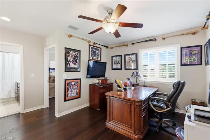 Versatile room featuring dark wood-finish flooring, a ceiling fan with integrated lighting, and a window with plantation shutters