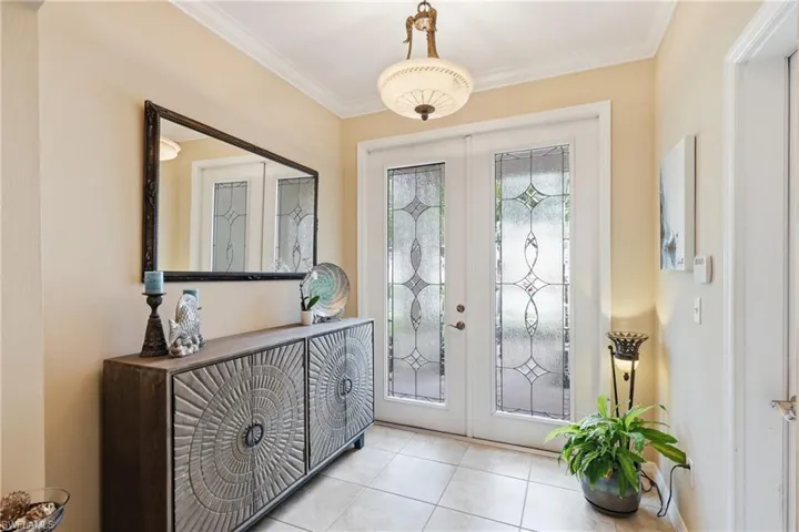 Entryway featuring double doors with decorative frosted glass inserts, crown molding, and tiled flooring