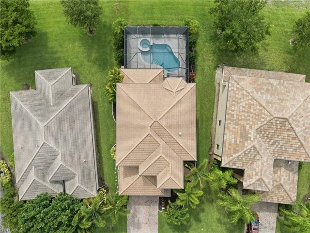 Tile-roof residence featuring a screened pool and spa, surrounded by mature landscaping and a well-maintained lawn
