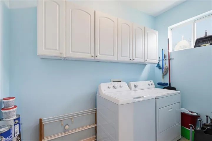 Dedicated laundry space featuring white cabinetry, a window, and light blue wall paint