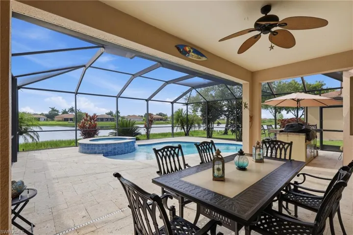Expansive screened lanai featuring a built-in outdoor kitchen, ceiling fan, and direct access to a private swimming pool with an integrated spa