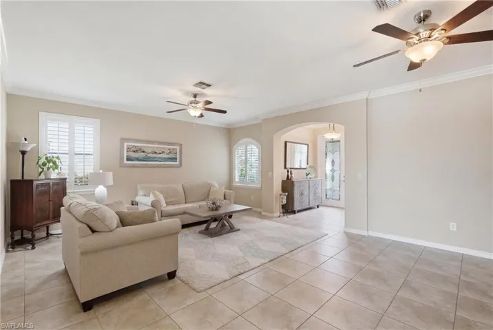 Spacious living area featuring tile flooring, crown molding, and multiple ceiling fans