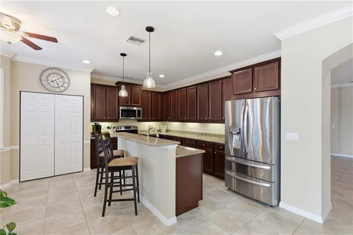 Kitchen featuring an island with counter seating, stainless steel appliances, dark wood cabinetry, recessed lighting, and tile flooring