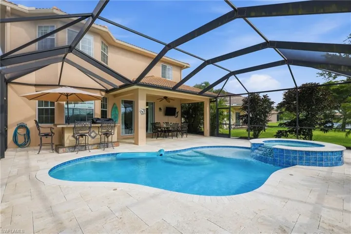 Screened outdoor living area featuring a freeform pool, integrated spa with waterfall, and a built-in outdoor kitchen with a stone-finish bar