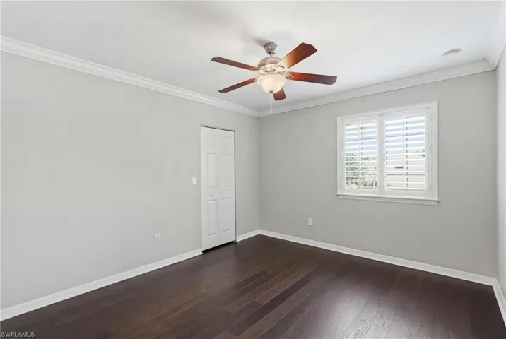 Room featuring dark wood-finish flooring, light grey walls, white baseboards, and crown molding