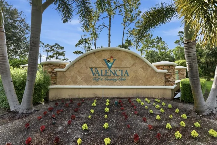 Stone and stucco monument sign featuring "Valencia Golf & Country Club" lettering, flanked by mature palm trees and manicured landscaping with ground cover