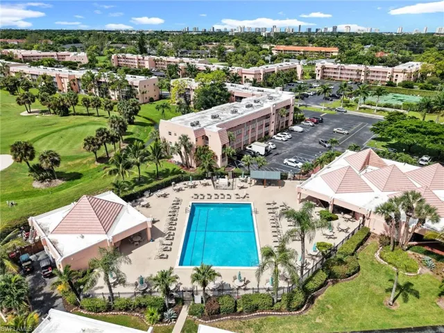 Community swimming pool and surrounding paved deck, adjacent to a golf course, parking area, and buildings
