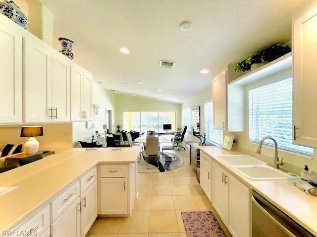 Kitchen with sink, light tile patterned floors, white cabinets, stainless steel dishwasher, and kitchen peninsula