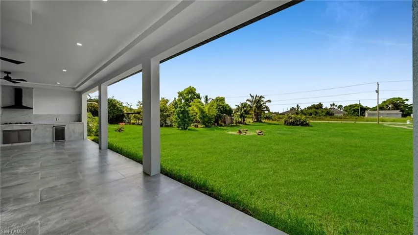 View of green lawn featuring a patio area, a ceiling fan, wine cooler, and exterior kitchen