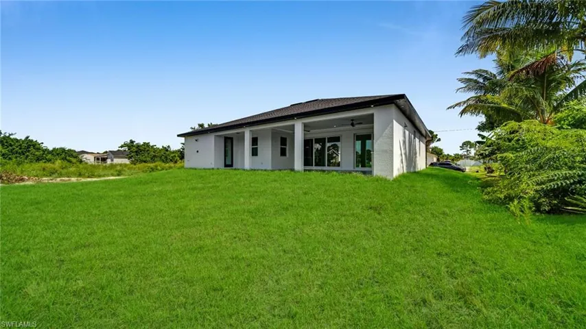 Back of house with stucco siding, a lawn, and a ceiling fan