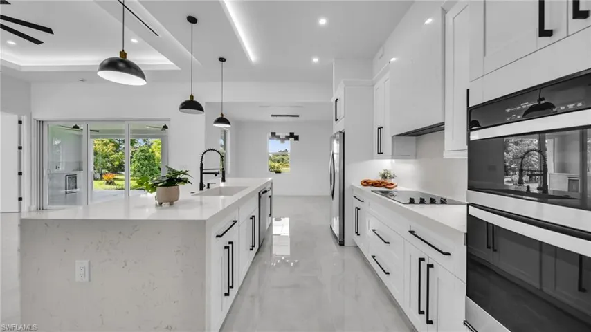 Kitchen with stainless steel appliances, ceiling fan, light marble finish flooring, white cabinetry, and an island with sink