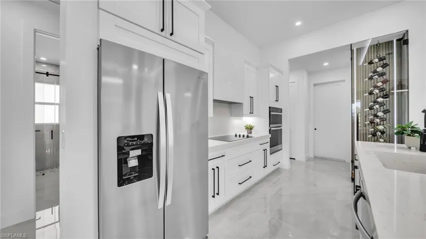 Kitchen with appliances with stainless steel finishes, white cabinetry, light marble finish flooring, recessed lighting, and light stone counters