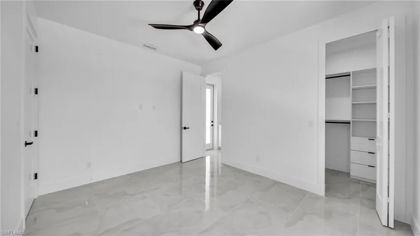 Unfurnished bedroom with light marble finish flooring, a spacious closet, and ceiling fan